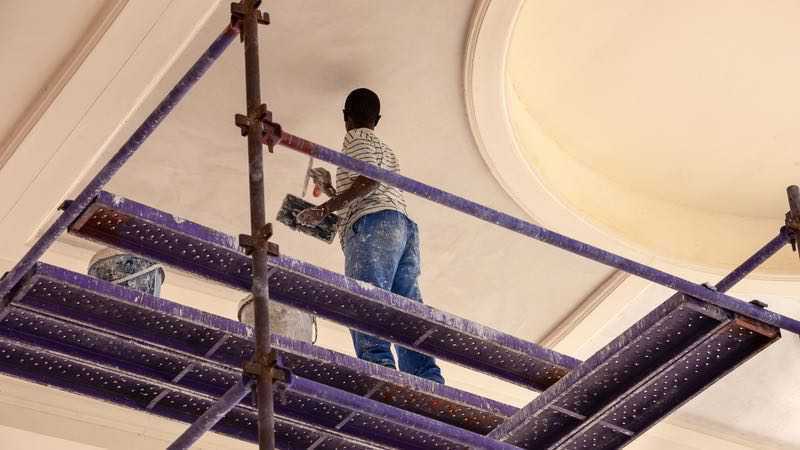 Plâtrier spécialiste de la finition sur échafaudage en train de plâtrer un plafond.