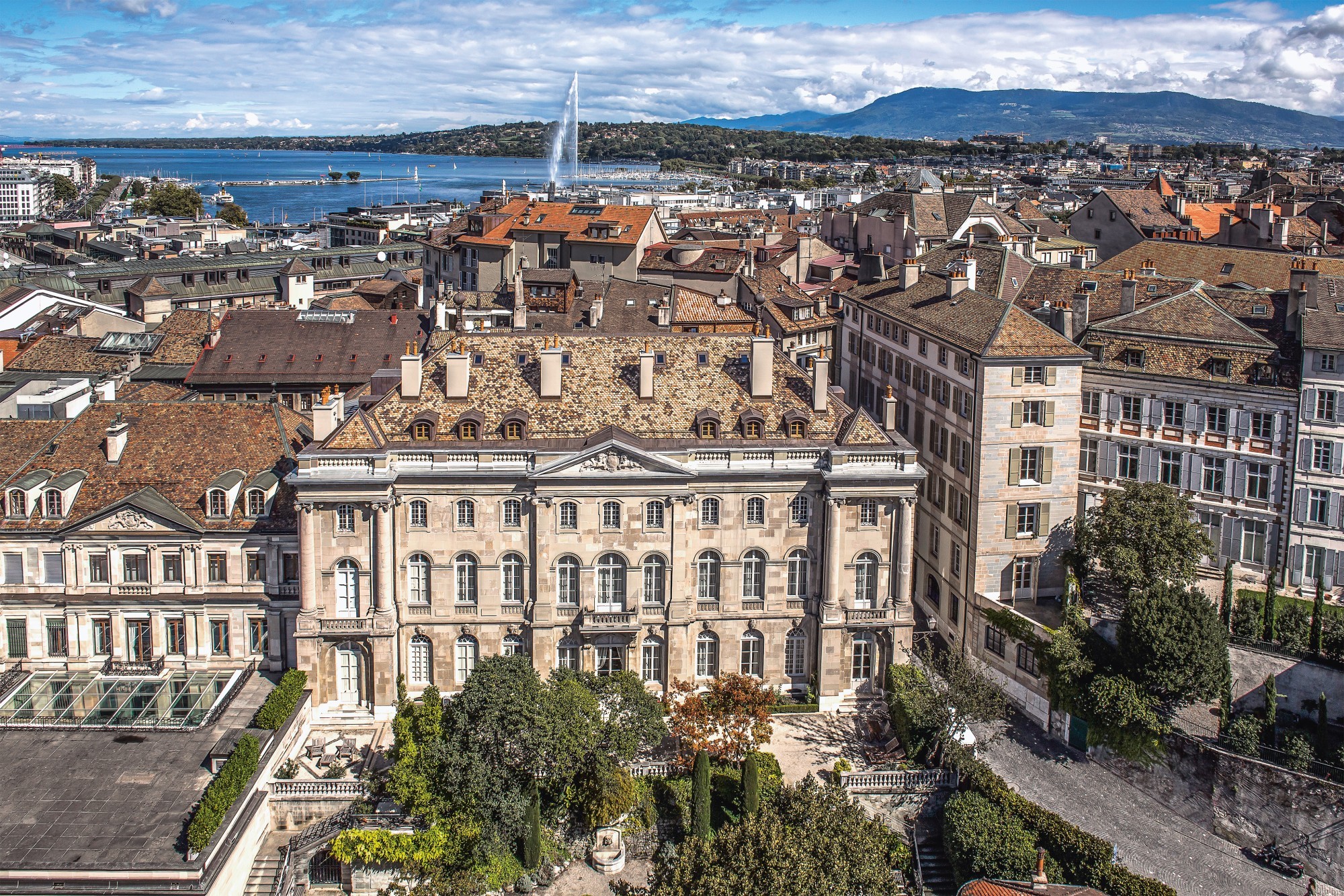 La Rue de la Cité 24 est un lieu emblématique à Genève. Vue sur l'Hôtel Lullin-de Saussure, avec sa façade majestueuse donnant sur le jardin et le front ouest de la haute ville. Au premier plan se trouve une série de bâtiments historiques alignés de gauch