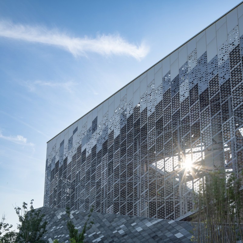 La lumière du soleil filtre à travers la façade perforée, conçue pour assurer la circulation de l’air vers les installations industrielles intérieures.
