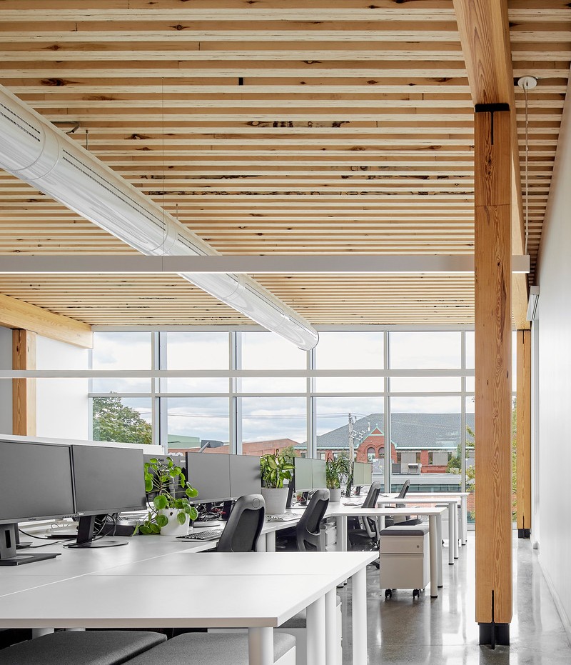 Le bois a été utilisé pour ses qualités structurelles, esthétiques et acoustiques. Le profil rainuré (ou en dents de scie) conçu pour les plafonds absorbe davantage le son qu'une surface plane, tout en ajoutant une composition architecturale rythmée.