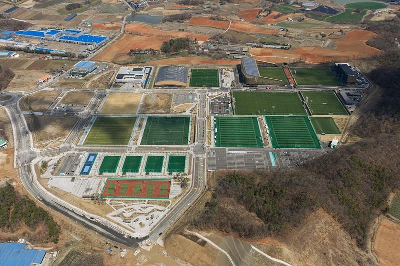 Le stade principal observé depuis les hauteurs, mettant en évidence la disposition des terrains, la structure du campus et la précision des volumes architecturaux.
