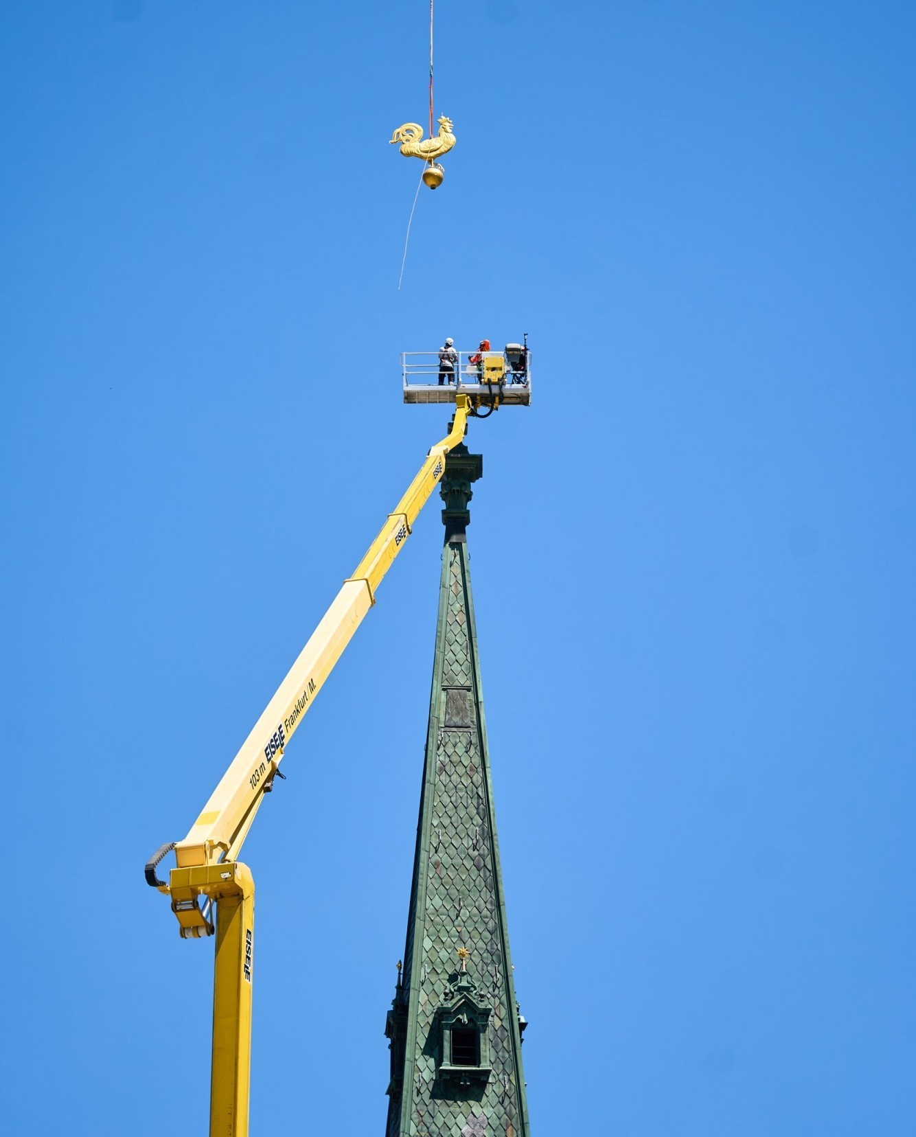 La girouette est suspendue au câble de l'hélicoptère, à 103 m d'altitude, et s'élève jusqu'au sommet du clocher.